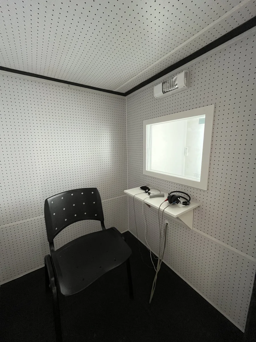 Interior da cabine de exame com cadeira e fones